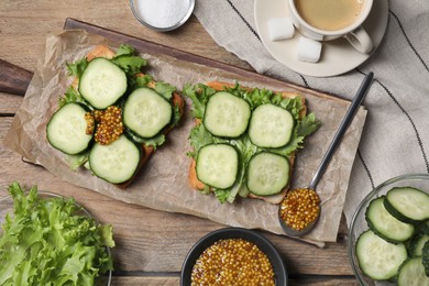 Photo of Tasty cucumber sandwiches with arugula and mustard on wooden table, flat lay