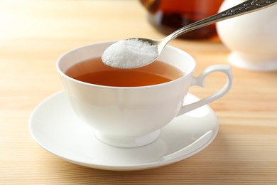 Photo of Adding sugar into cup of tea at wooden table, closeup