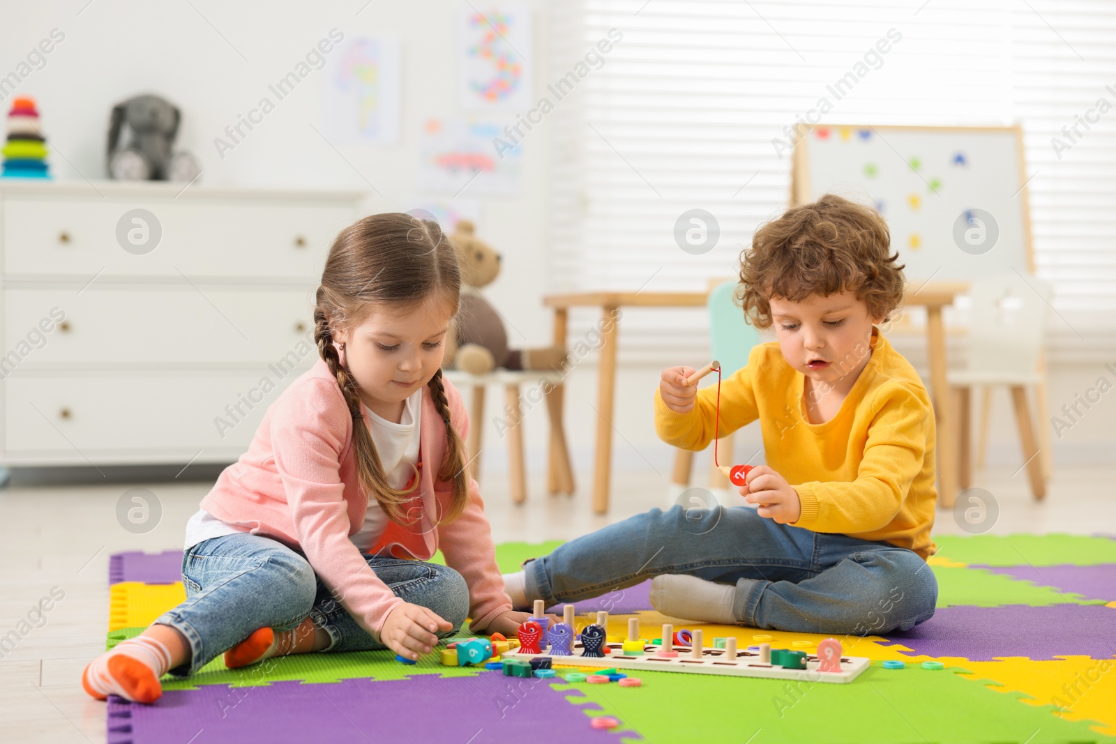 Photo of Cute little children playing with math game Fishing for Numbers on puzzle mat in kindergarten