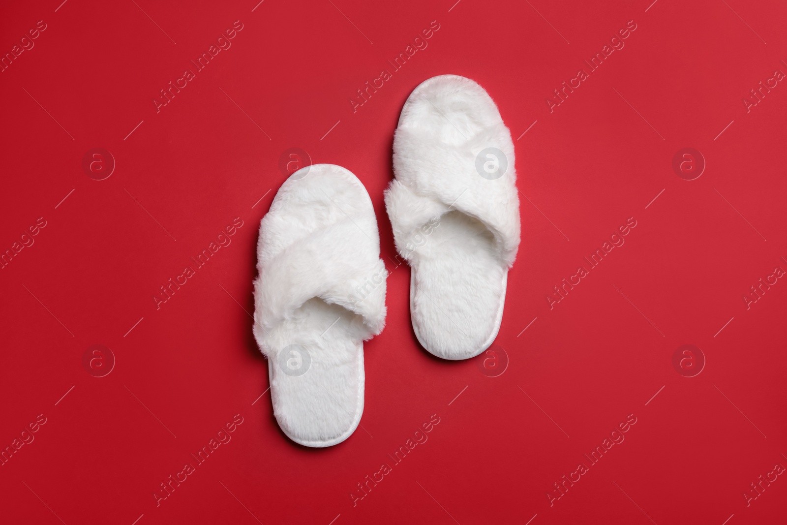Photo of Pair of soft white slippers on red background, top view