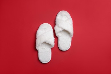 Photo of Pair of soft white slippers on red background, top view
