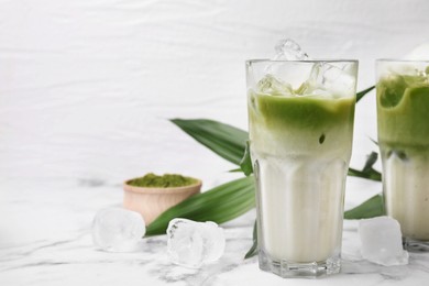 Photo of Glasses of tasty iced matcha latte and leaves on white marble table. Space for text