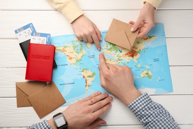 Man and woman planning their honeymoon trip with world map at white wooden table, top view