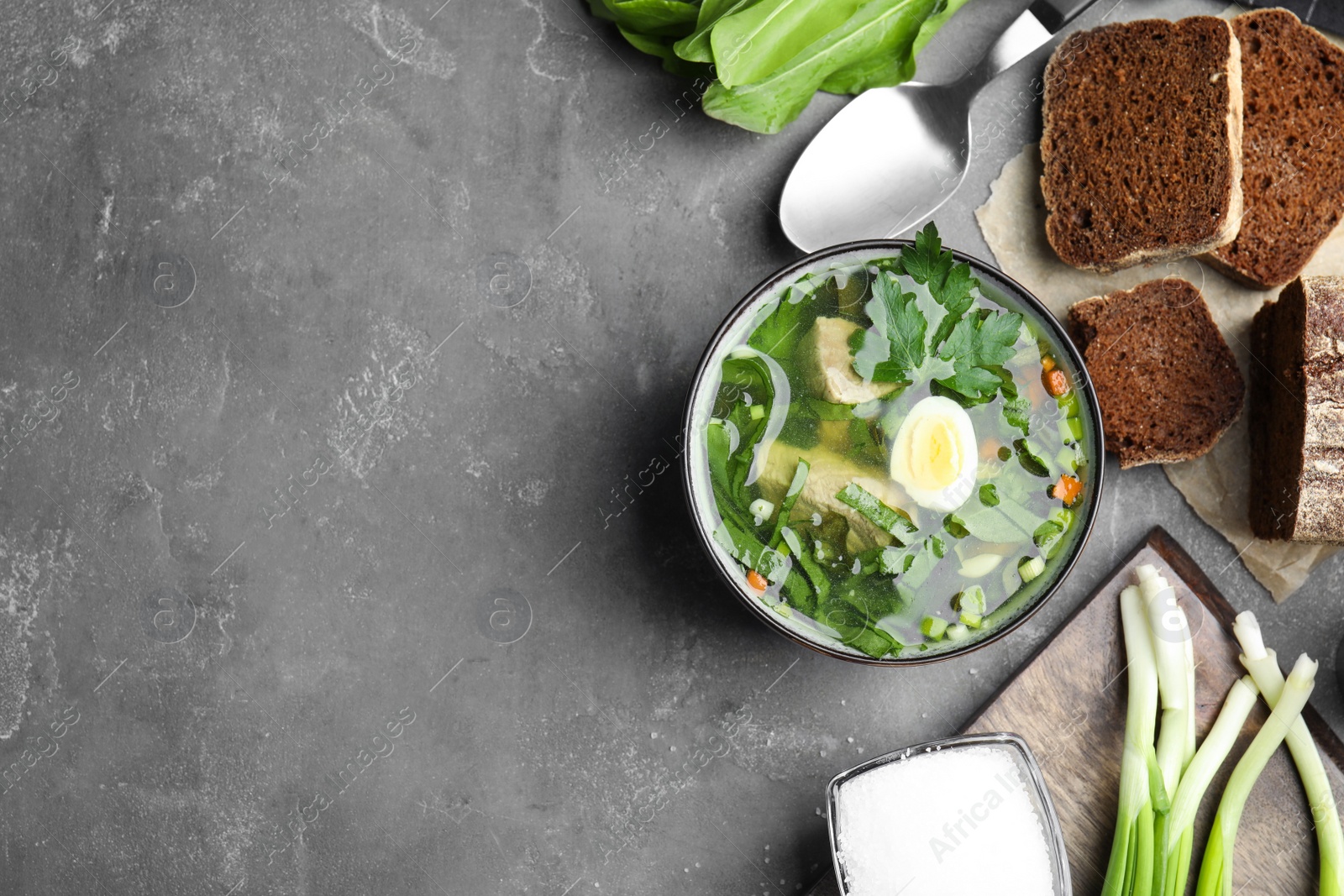 Photo of Delicious sorrel soup with meat and egg served on grey table, flat lay. Space for text