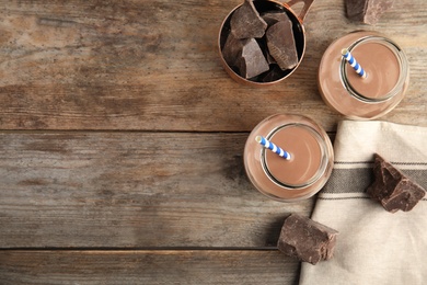 Flat lay composition with jars of tasty chocolate milk and space for text on wooden background. Dairy drink