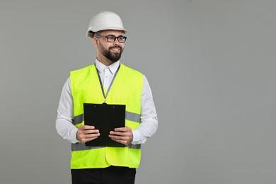 Photo of Engineer in hard hat holding clipboard on grey background, space for text