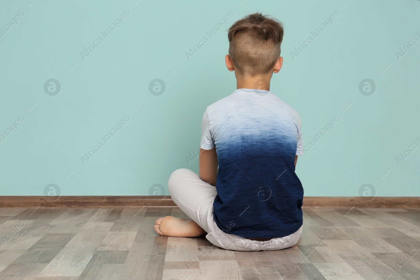 Photo of Little boy sitting on floor near color wall in empty room. Autism concept