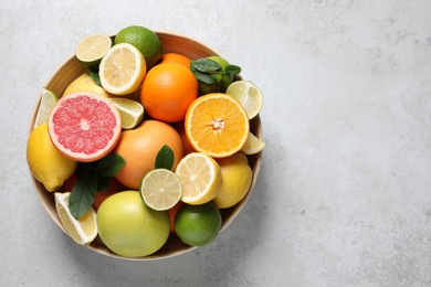 Photo of Different fresh citrus fruits and leaves in bowl on light table, top view. Space for text