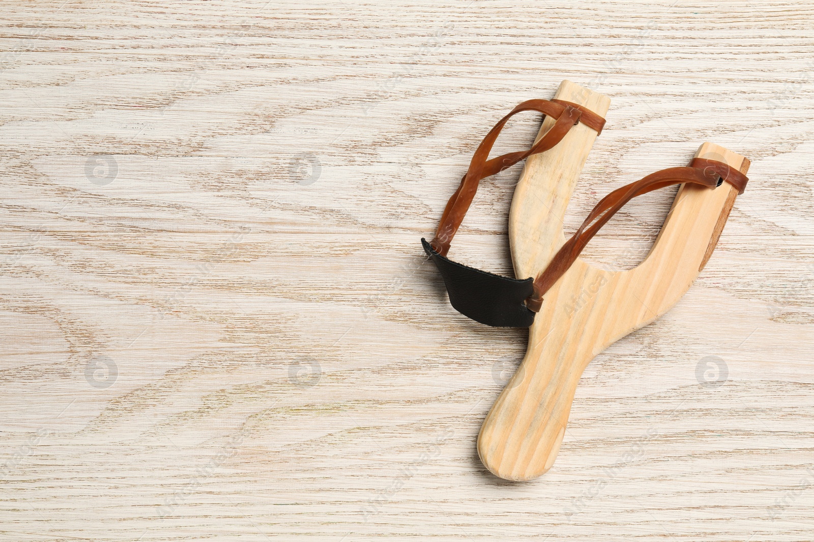 Photo of Slingshot with leather pouch on wooden background, top view. Space for text