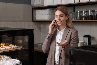 Photo of Happy business owner talking on phone in bakery shop