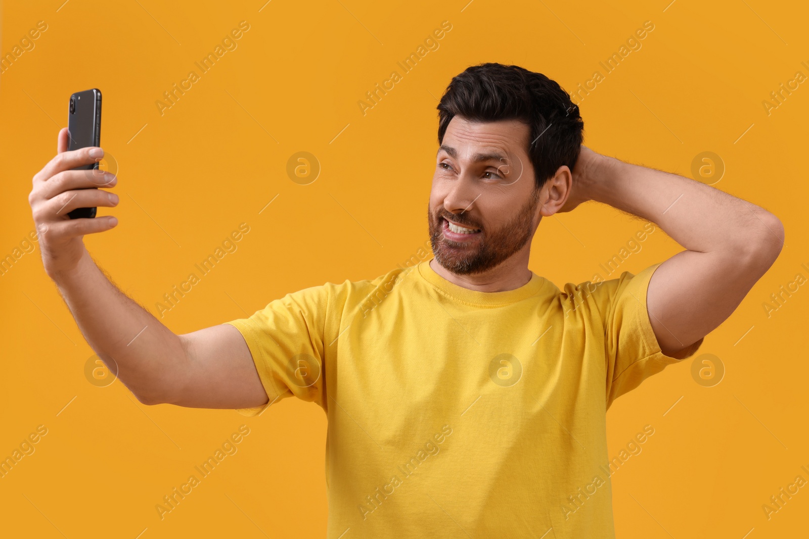Photo of Emotional man taking selfie with smartphone on yellow background