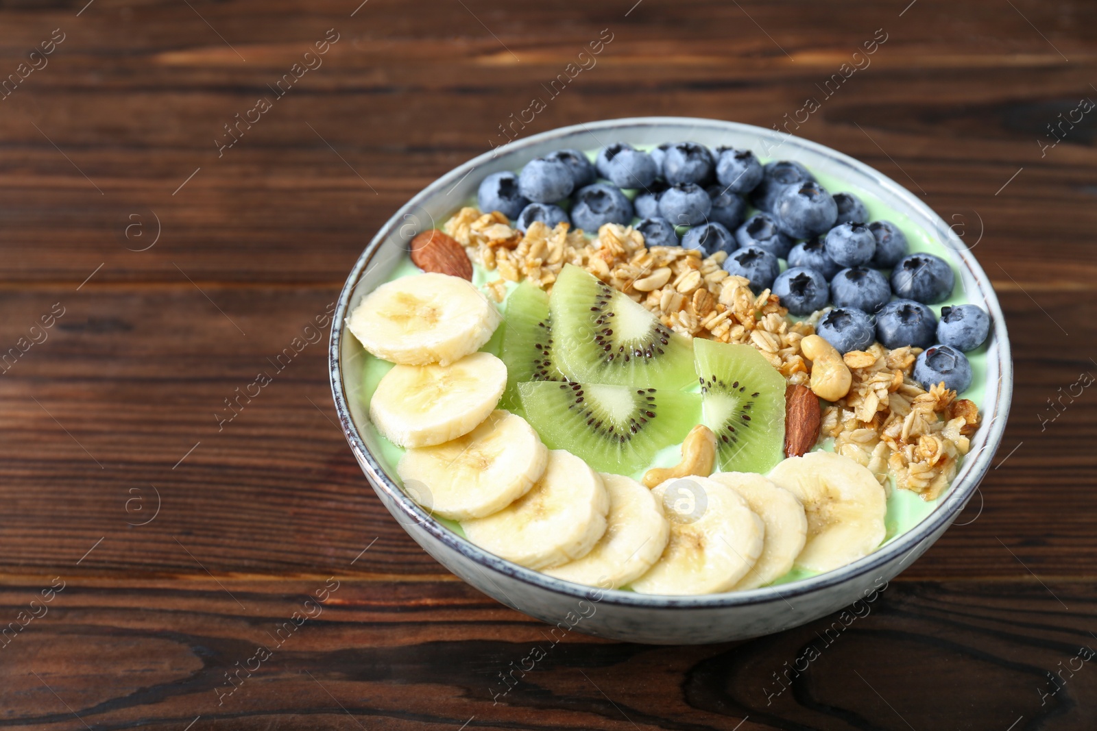 Photo of Tasty smoothie bowl with fresh fruits and oatmeal on wooden table, space for text