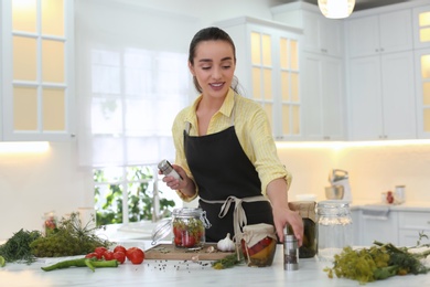 Woman adding seasonings to vegetables in pickling jar at kitchen table