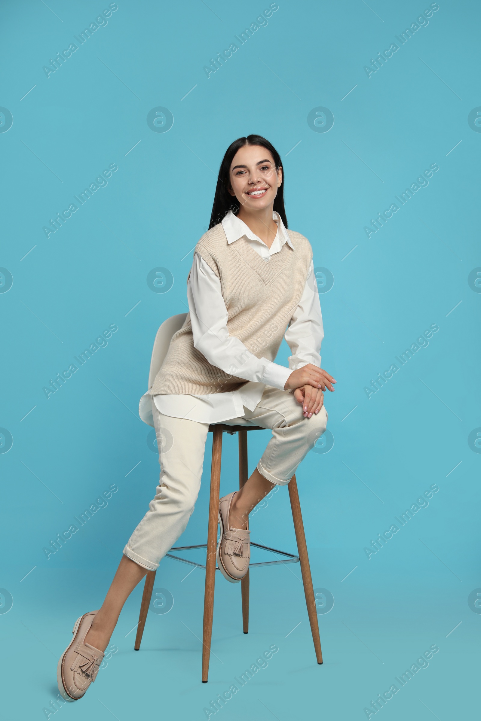 Photo of Beautiful young woman sitting on stool against turquoise background