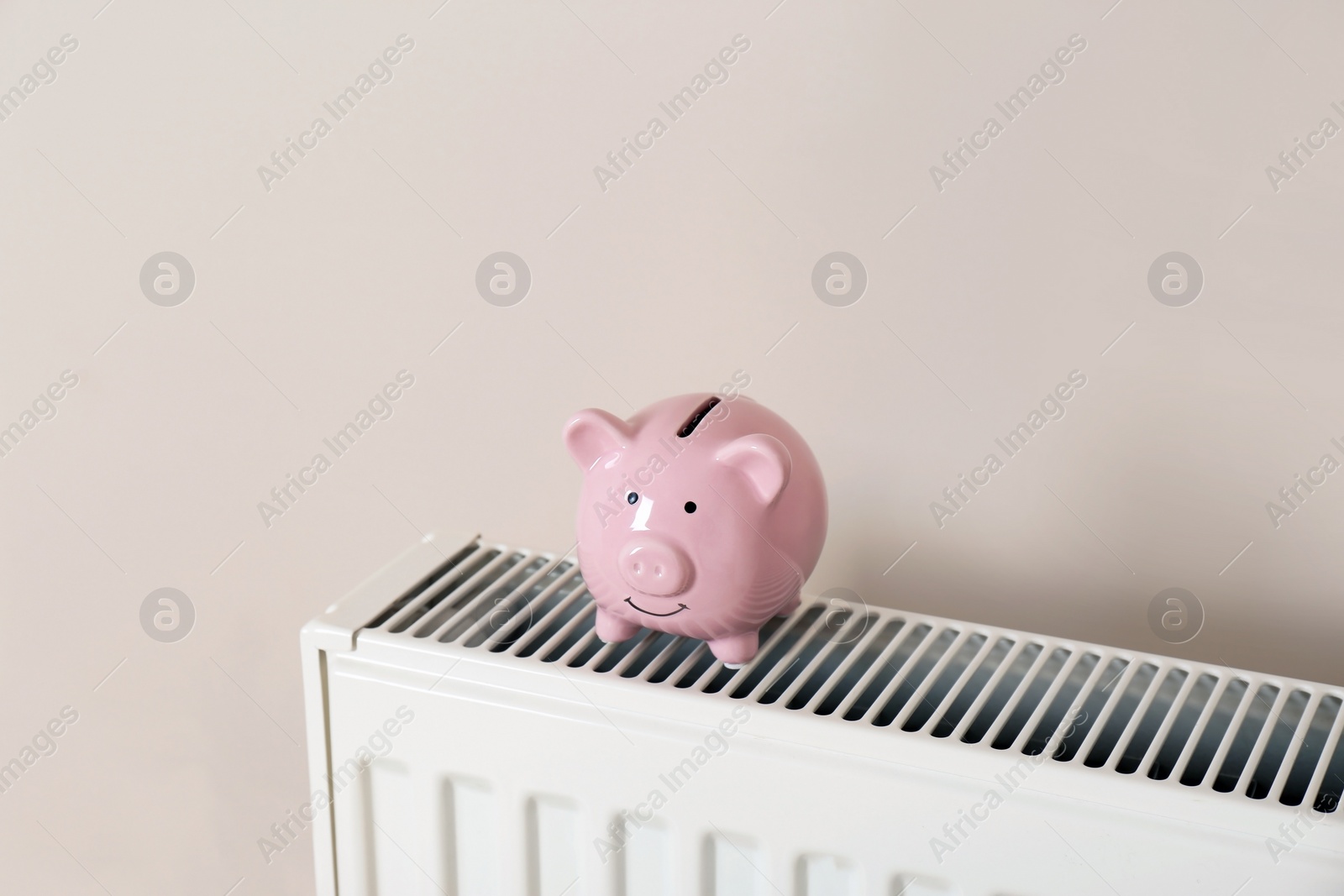 Photo of Piggy bank on heating radiator against light background