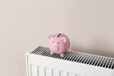 Piggy bank on heating radiator against light background