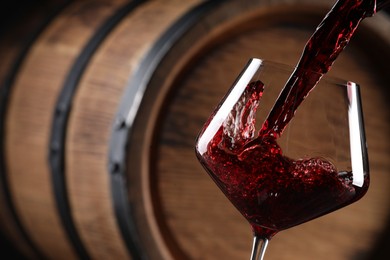 Pouring red wine into glass near wooden barrel, closeup. Space for text