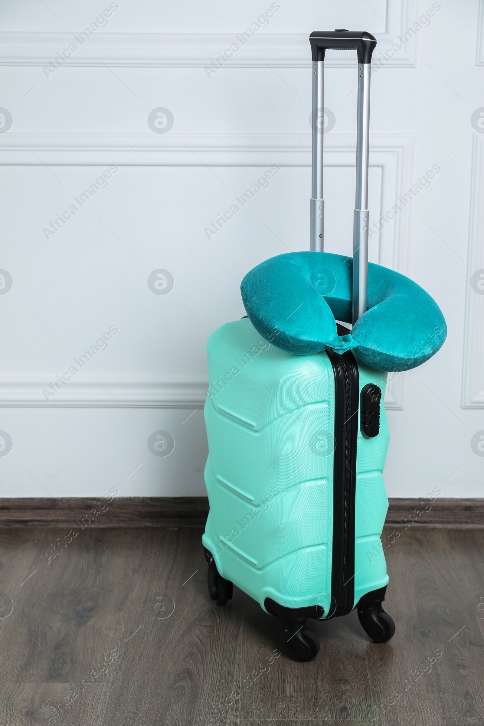 Photo of Turquoise travel pillow on suitcase near white wall indoors