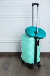 Photo of Turquoise travel pillow on suitcase near white wall indoors