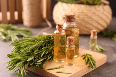 Photo of Essential oil in bottles and rosemary on grey table