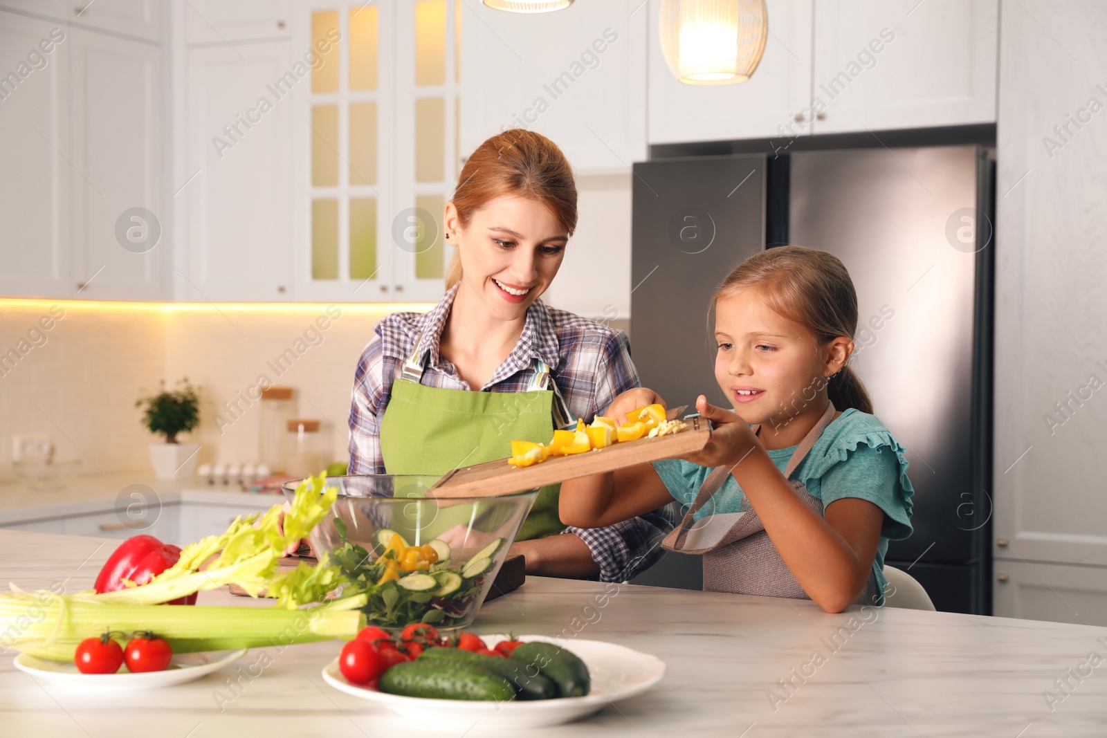 Photo of Mother and daughter cooking salad together in kitchen