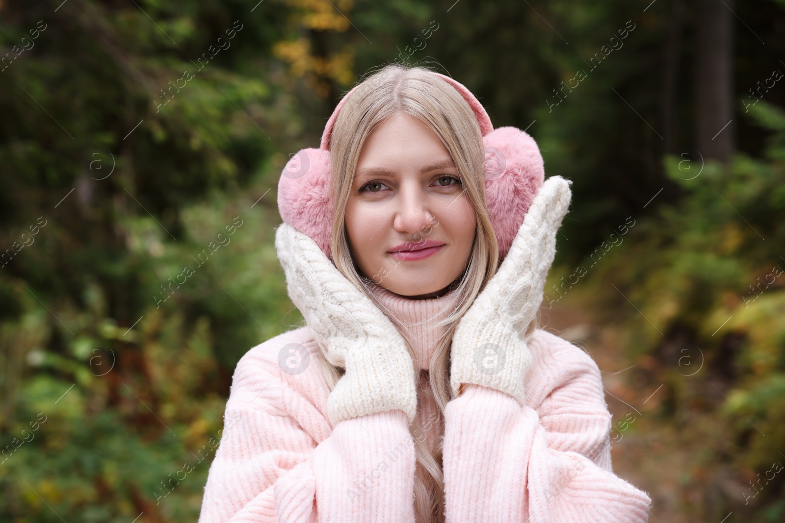 Photo of Young beautiful woman wearing warm earmuffs in forest