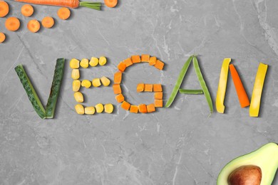 Image of Word VEGAN made of different fresh tasty vegetables on light grey marble background, flat lay