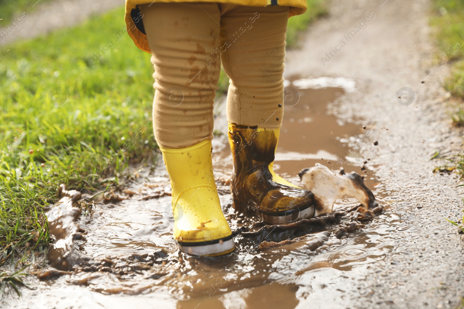 Photo of Little girl wearing rubber boots walking in puddle, closeup
