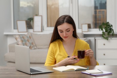 Photo of Woman with cup of coffee and notebook at wooden table indoors