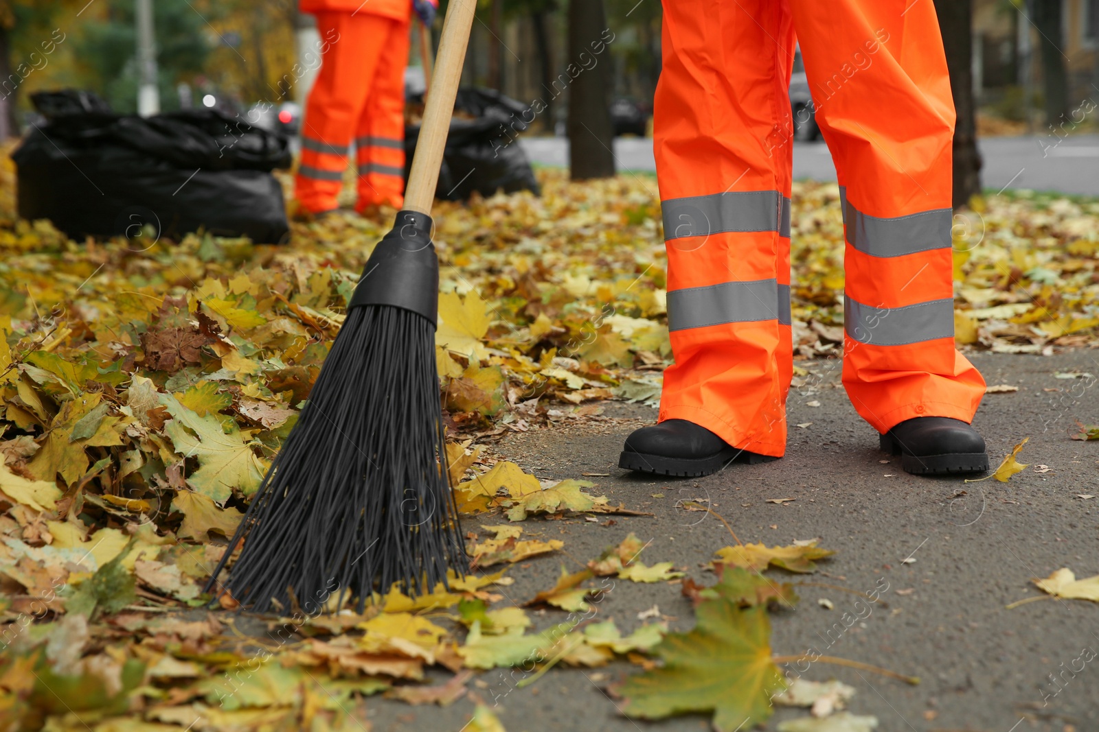 Photo of Street cleaners sweeping fallen leaves outdoors on autumn day, closeup