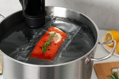 Sous vide cooker and vacuum packed salmon in pot on table, closeup. Thermal immersion circulator