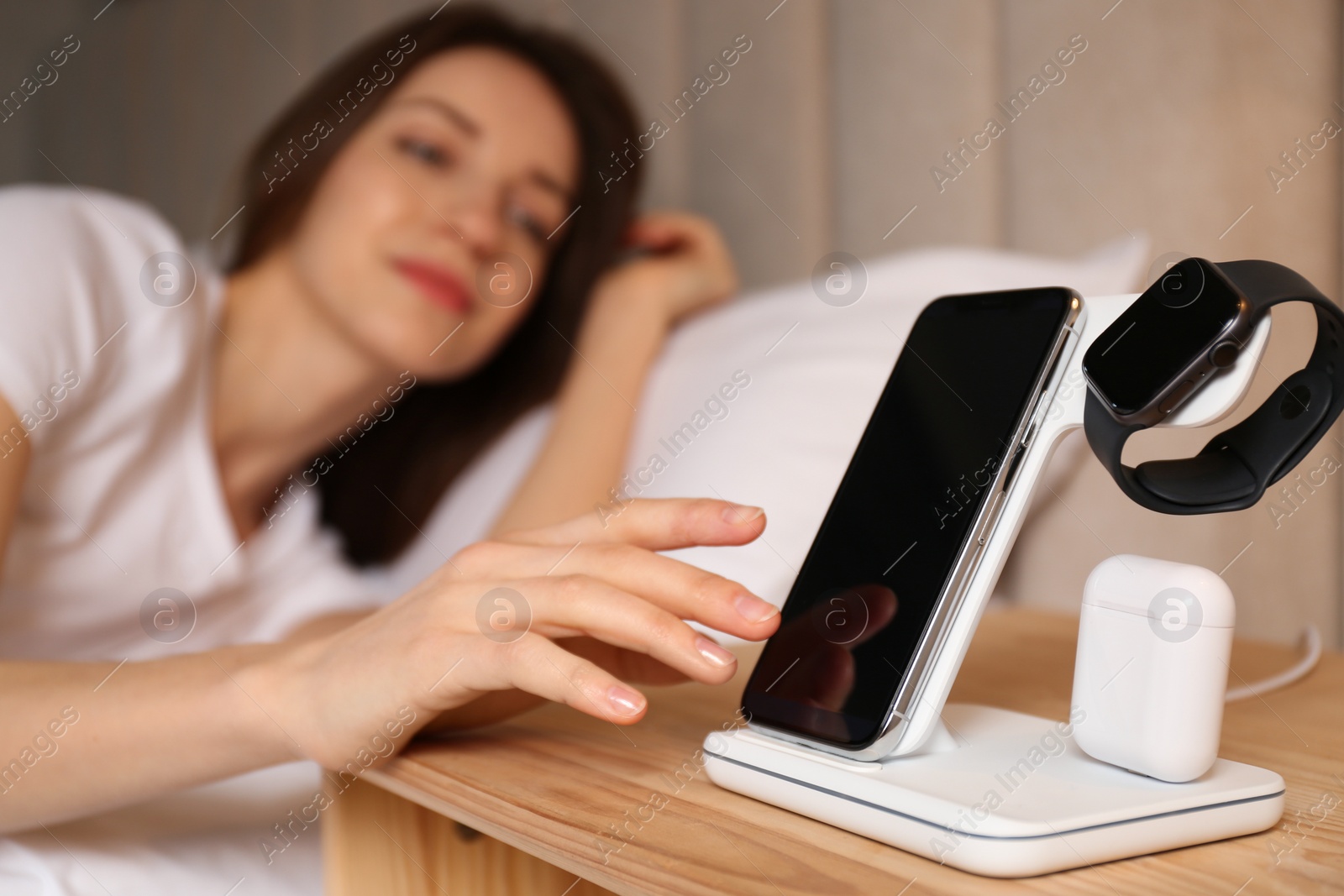 Photo of Woman taking smartphone from wireless charger in bedroom