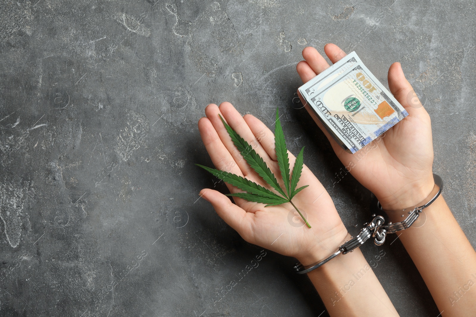 Photo of Woman in handcuffs holding hemp leaf and dollars on grey stone background, closeup. Space for text