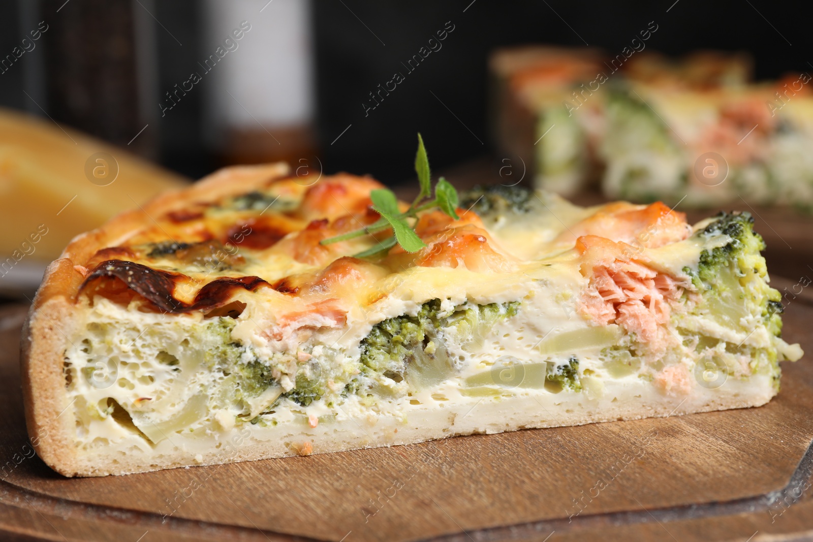 Photo of Piece of delicious homemade quiche with salmon and broccoli on wooden board, closeup