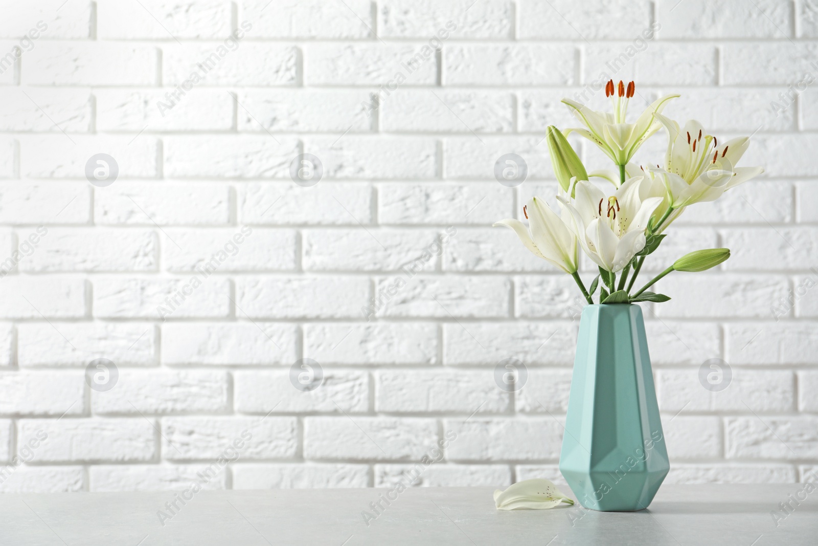 Photo of Vase of beautiful lilies on table against  white brick wall, space for text