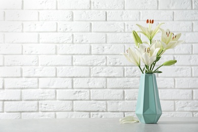 Photo of Vase of beautiful lilies on table against  white brick wall, space for text