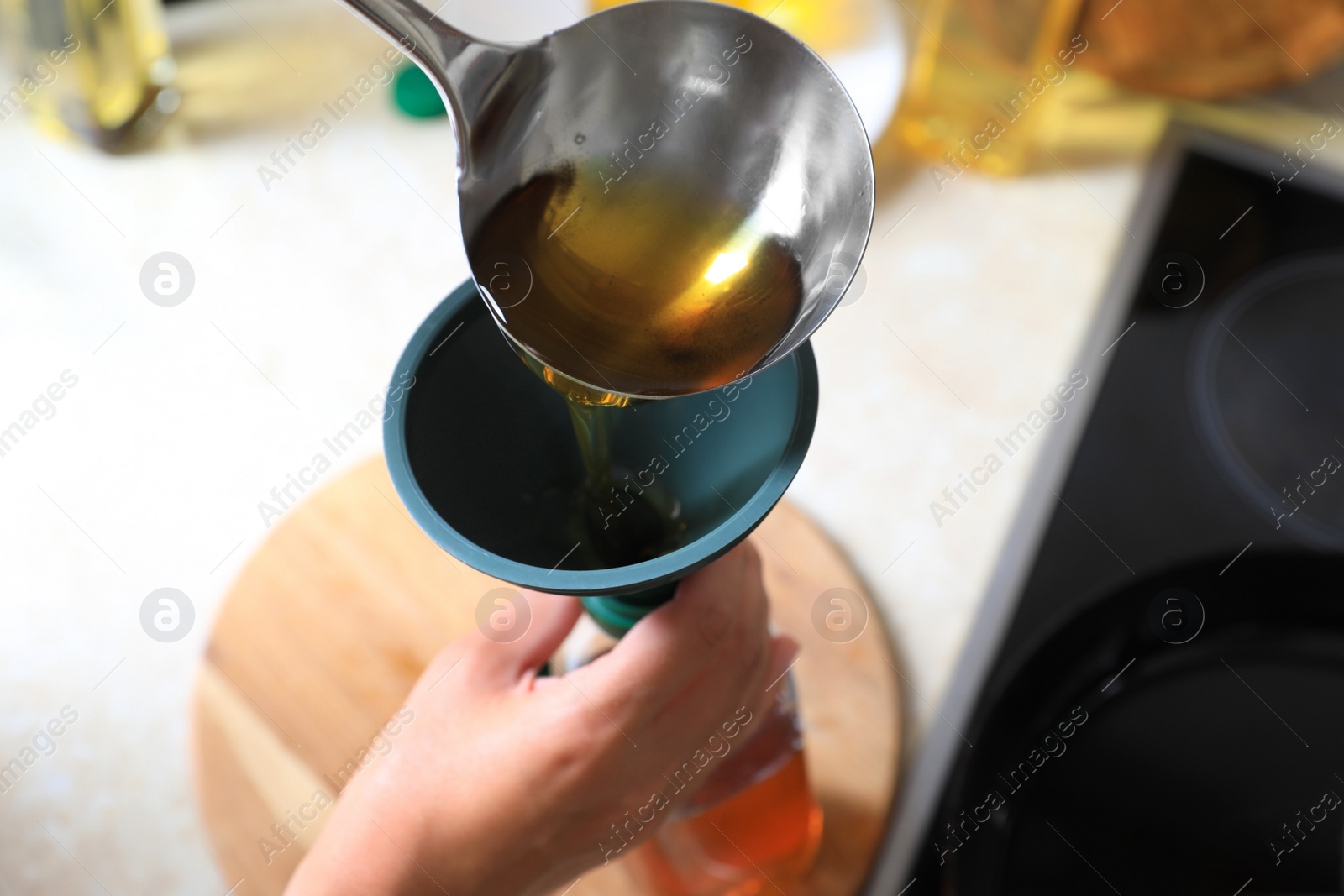 Photo of Woman pouring used cooking oil into bottle through funnel in kitchen, closeup