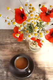 Beautiful bouquet of poppies and chamomiles near cup with coffee indoors, focus on flowers