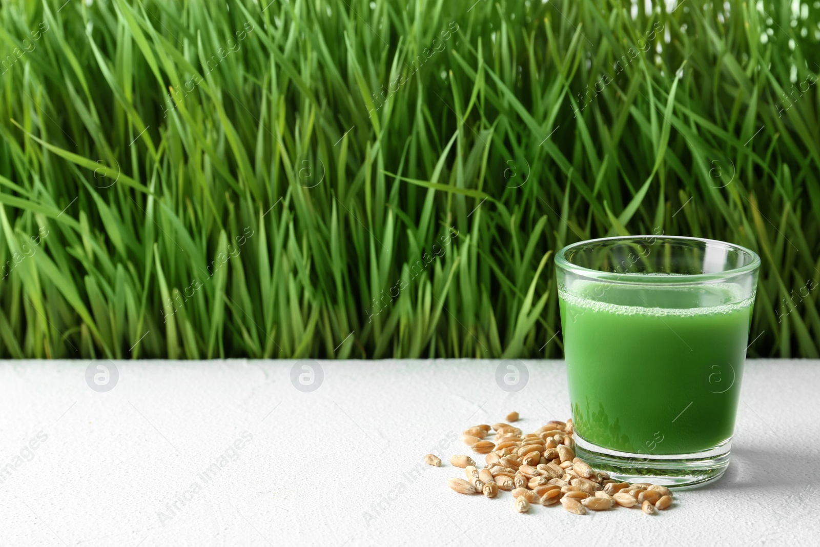 Glass of juice and grains on table near fresh wheat grass. Space for text Photo of Glass of juice and grains on table near fresh wheat grass. Space for text