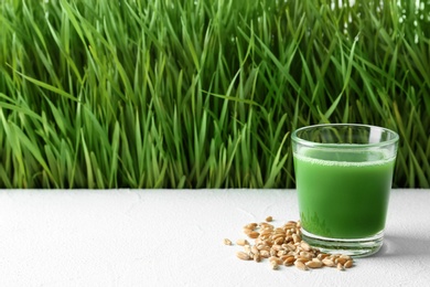 Photo of Glass of juice and grains on table near fresh wheat grass. Space for text