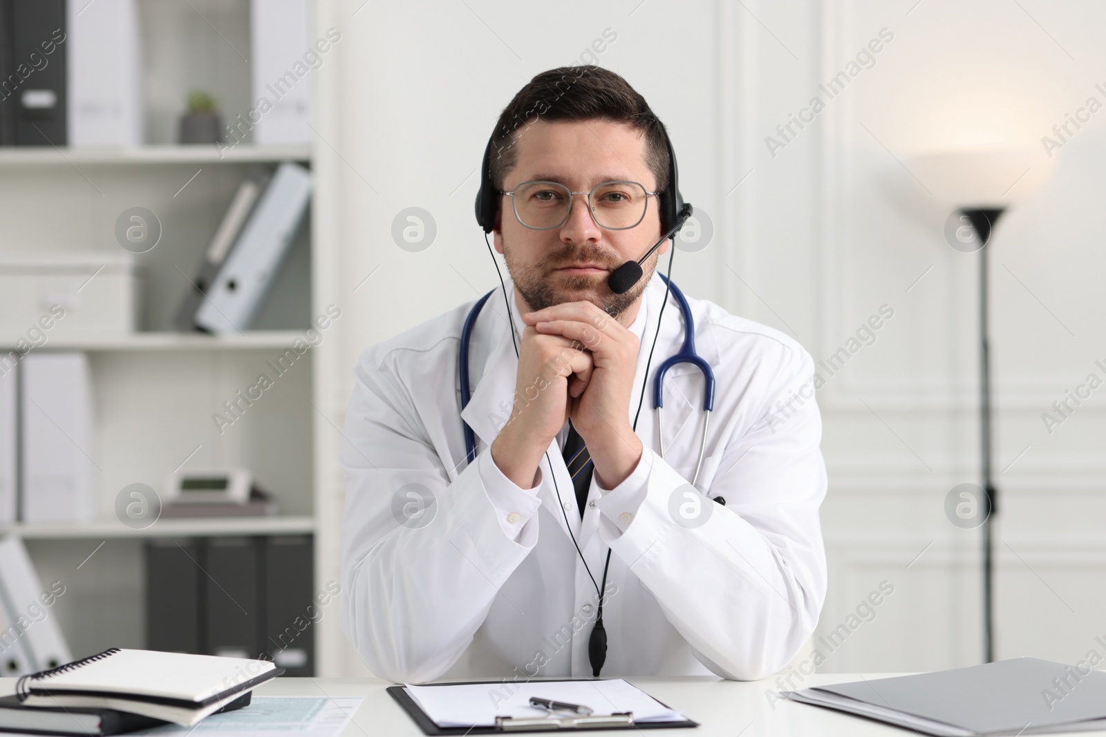 Photo of Doctor in headset having online consultation at table in clinic