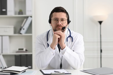 Doctor in headset having online consultation at table in clinic