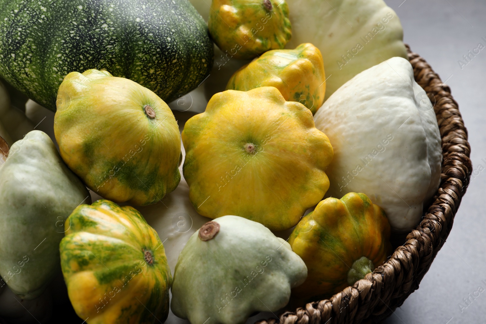 Photo of Fresh ripe pattypan squashes in wicker bowl on table, closeup