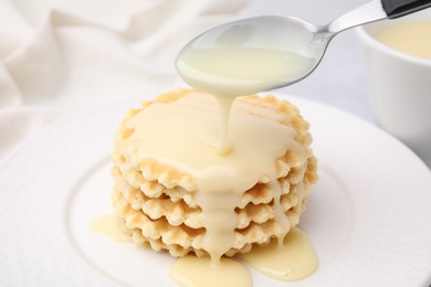 Photo of Pouring tasty condensed milk onto waffles on table, closeup