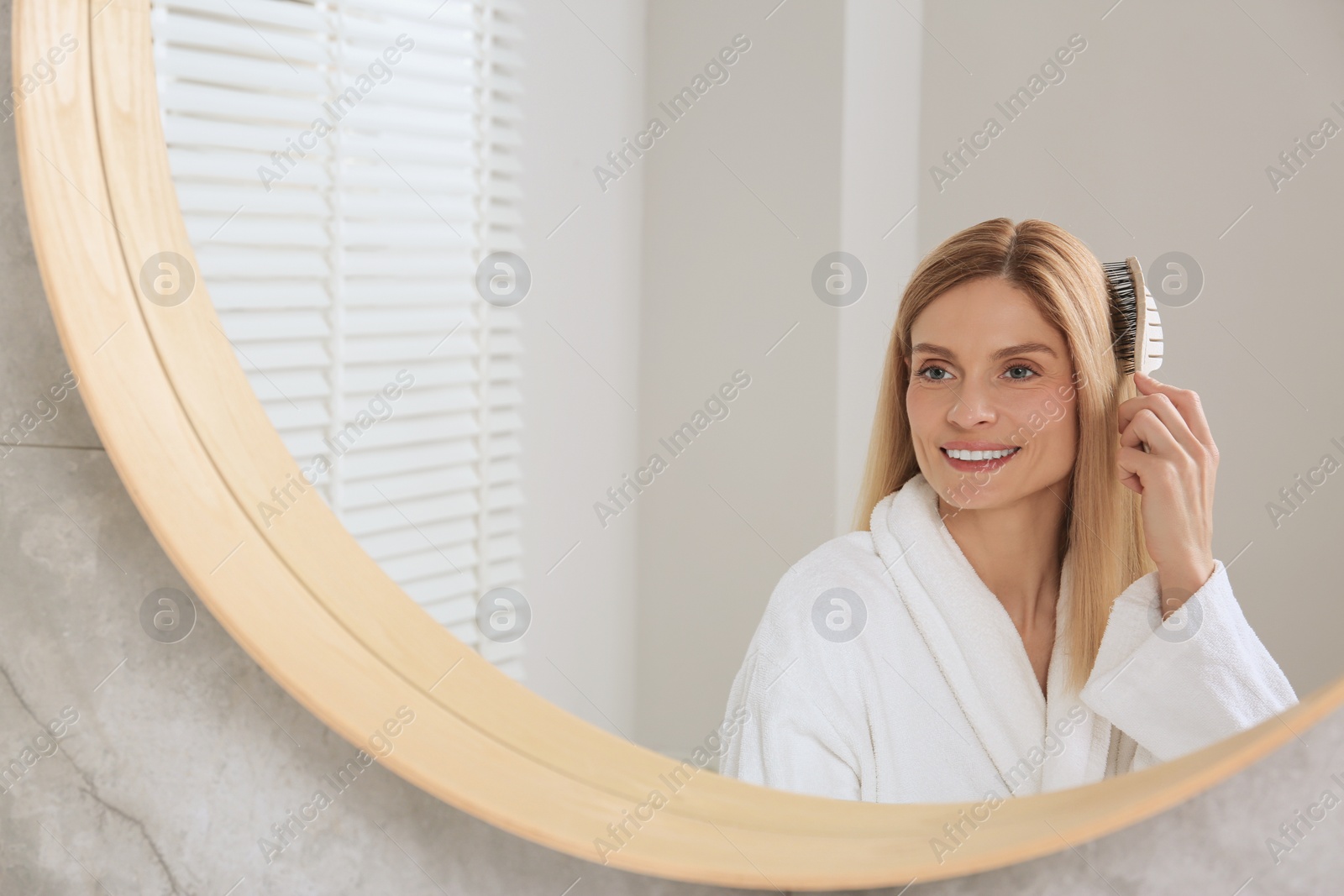 Photo of Beautiful woman brushing her hair near mirror in bathroom