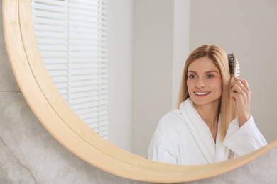 Beautiful woman brushing her hair near mirror in bathroom
