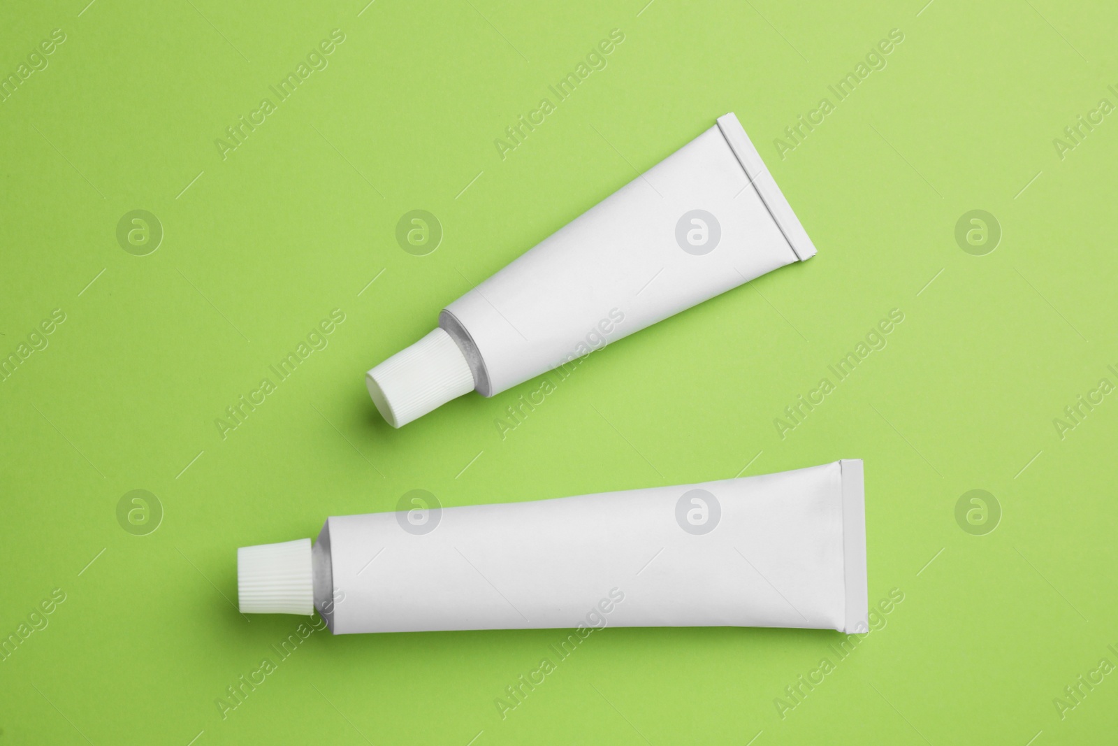 Photo of Blank white tubes of ointment on light green background, flat lay. Space for text