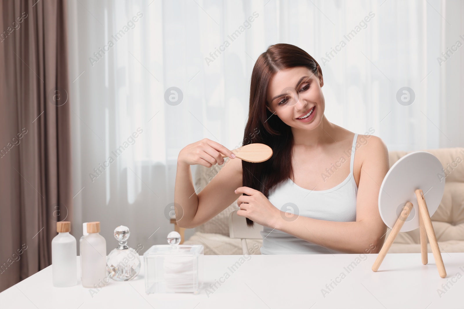 Photo of Beautiful woman brushing her hair near mirror in room, space for text