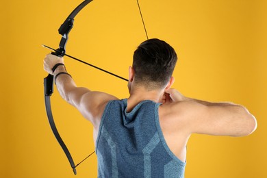 Man with bow and arrow practicing archery on yellow background, back view