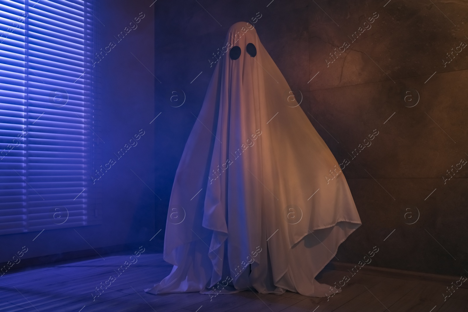 Photo of Creepy ghost. Woman covered with sheet near window in color lights